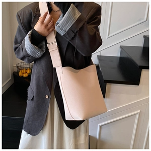 Sac seau en cuir rose pâle avec large bandoulière porté par un mannequin sur un escalier