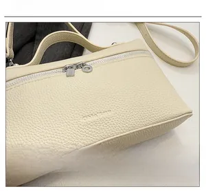 Macro shot of beige lychee grain leather handbag with embossed logo and silver zipper