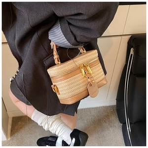 Detail of handwoven straw box bag with brown leather handles and gold zippers worn by model
