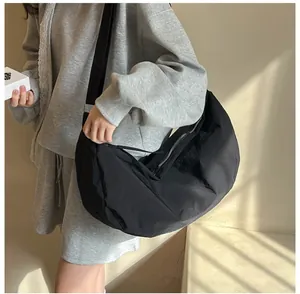 Minimalist black nylon crescent crossbody bag shown with wide shoulder strap on model