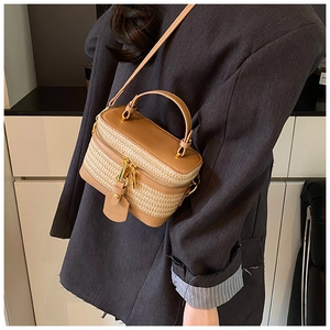 Detail of hand-woven straw box bag with brown faux leather trim and gold hardware accents