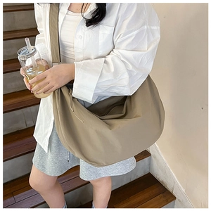 Detail view of a large khaki nylon crescent bag with wide strap worn by a model