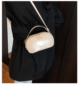 Detail of a creamy beige leather handbag with double zipper and top handle shown on a black blazer