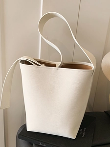 Sac seau minimaliste en cuir grainé beige avec bandoulière large sur fond décoratif