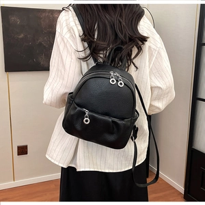 Close-up of litchi grain texture and silver ring zippers on a small black backpack