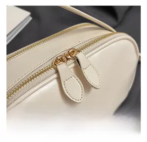Detailed close-up of golden dual zippers on a sleek cream oil wax leather crossbody bag