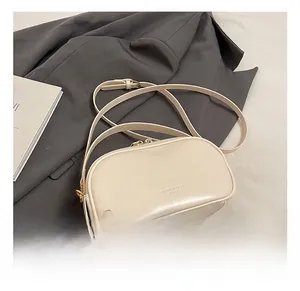 Detailed close-up of cream leather crossbody bag with logo on a grey blazer