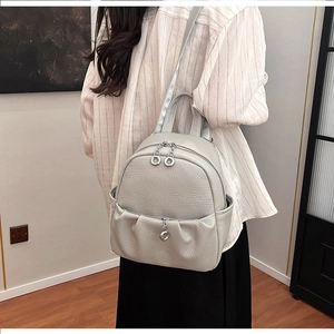 Detailed view of light gray lychee texture backpack with metallic ring zippers on model