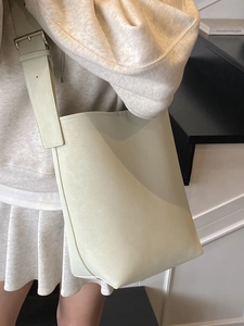Sac seau minimaliste en cuir beige avec large bandoulière réglable et détails argentés