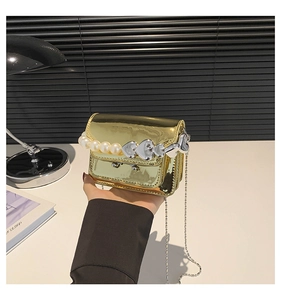Close-up of golden metallic mini bag with pearl and heart handle detail in scene