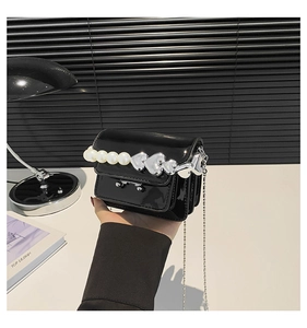 Close-up of black patent leather mini bag with pearl heart charm and silver chain strap