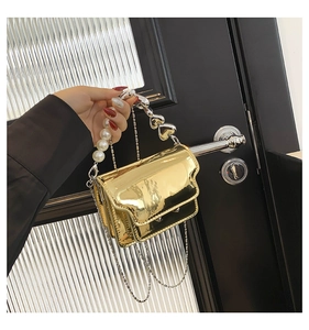 Detail of mini gold metallic bag featuring pearl handle, heart rings and fine chain strap