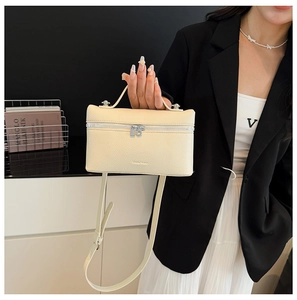 Close-up of beige lychee grain leather box bag with top handle and silver metal zipper