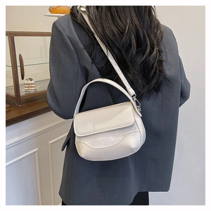 Rear view of model holding cream saddle bag with adjustable strap in minimalist cafe