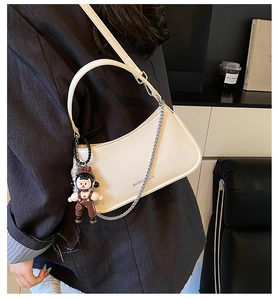 Detail of white leather crescent bag with metal chain decoration and cute doll pendant