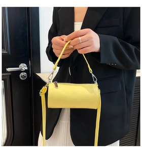 Detail einer leuchtend gelben Zylindertasche mit abnehmbarem Gurt und Lederstruktur