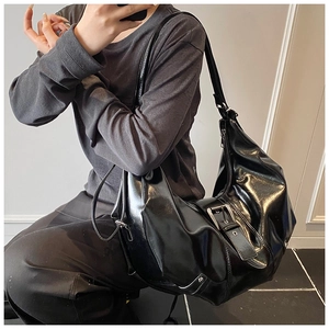 Close-up of a glossy black tote bag featuring metallic buckles and premium leather texture