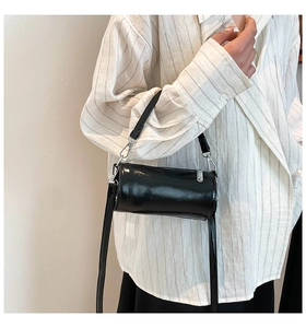 Detail einer schwarzen glänzenden Zylindertasche mit Silber-Reißverschluss und Schultergurt