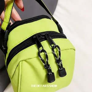 Detail shot of lime green nylon crossbody bag featuring dual zippers and durable paracord pulls