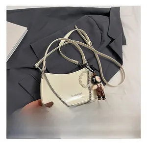 Detail of cream patent leather bag with silver chain, pearl strap and character charm
