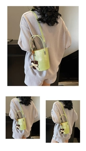 Close-up of light green bucket bag featuring a lace bow pendant and long shoulder strap