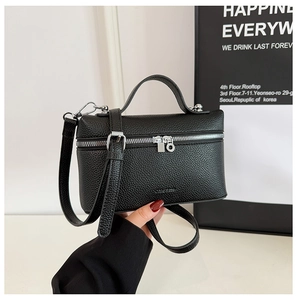 Detail of black pebbled leather texture and silver dual zippers on boxy handbag