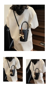 Detailed view of black leather bucket bag with lace bow charm on dark staircase background
