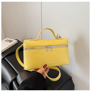 Detail of a bright yellow lychee texture square bag with silver double zippers and strap