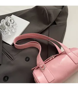 Pink PU leather cylindrical baguette bag with wide shoulder strap on dark blazer background