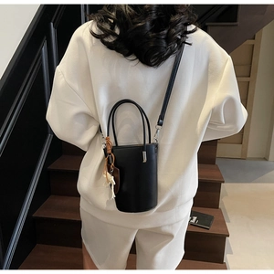 Detail of a black leather bucket bag with tassel charm worn over a white hoodie