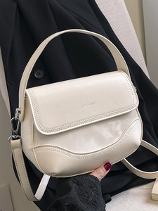 Minimalist beige leather saddle bag with silver hardware held against black blazer