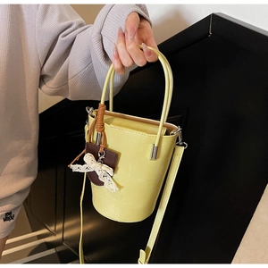 Close-up of a yellow bucket bag with a lace bow and brown charm, held by a model