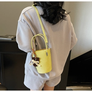 Detail of bright yellow bucket bag with lace bow and leather tag on a stylish model