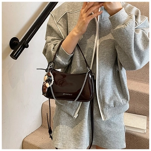 Detail of dark brown patent leather shoulder bag with silver chain and astronaut charm