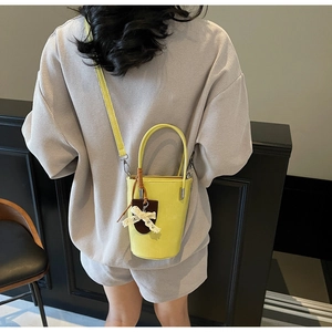 Detail of yellow bucket bag with brown tag and lace bow accessory on gray outfit