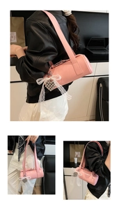 Detail of pink cylindrical baguette bag featuring a heart pendant and lace bow detail