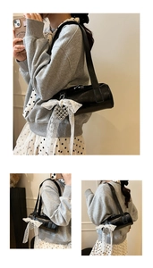 Detail of black cylindrical baguette bag with large white lace bow and heart charm