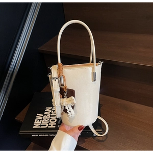 Detail of white bucket bag with lace bow and brown leather tag on a wooden background