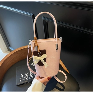 Detailed shot of a pink bucket bag featuring a white lace bow and leather charm accessory