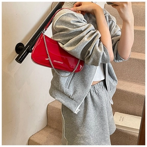 Detail of red patent leather shoulder bag with metallic chain strap and zipper