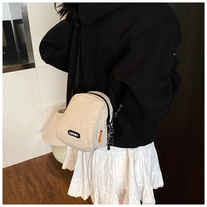 Detail view of beige nylon crossbody bag featuring Lucky patch and orange side label detail