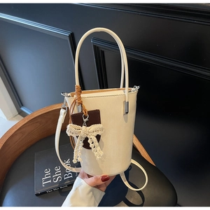 Close-up of cream bucket bag with lace bow pendant and adjustable strap on a chair