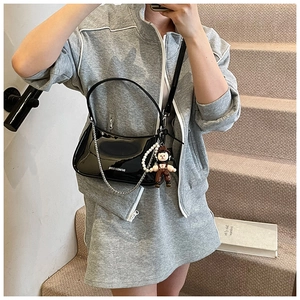 Detail of black patent leather underarm bag with silver chain and cute doll charm accessory
