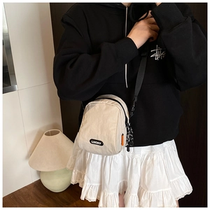 Close-up of cream nylon crossbody bag with Lucky logo worn by a model in casual style