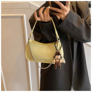 Close-up of yellow patent leather baguette bag with silver chain and cute doll charm