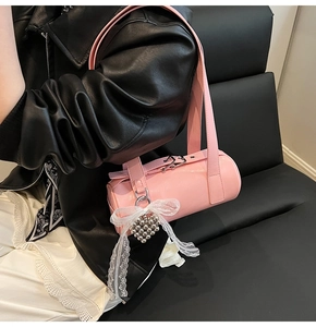 Close-up of pink barrel bag with lace bow pendant and metallic heart charms on a leather seat