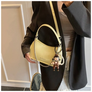 Detail of pale yellow patent leather hobo bag with silver chain and cute doll charm
