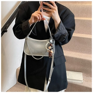 Detail of silver patent leather shoulder bag with decorative chain and doll pendant charms