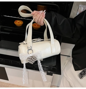 Close-up of cream Boston bag with lace bow and heart charm in a warm bakery setting