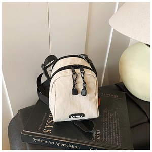 Detail view of the beige nylon mini crossbody bag with LUCKY label resting on a black book